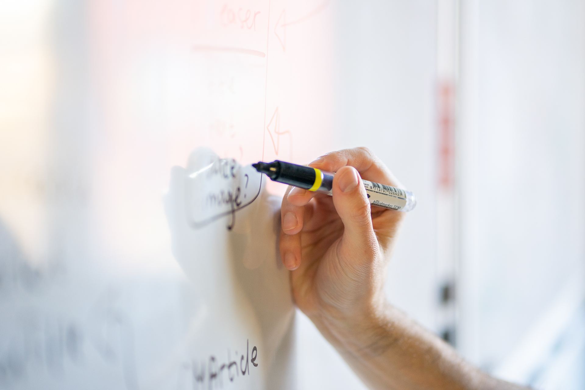 Nahaufnahme von einer Hand die mit einem Stift etwas an eine Wandtafel schreibt